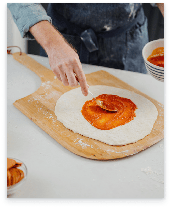 Greg Gall applies pizza sauce on top of pizza dough.
