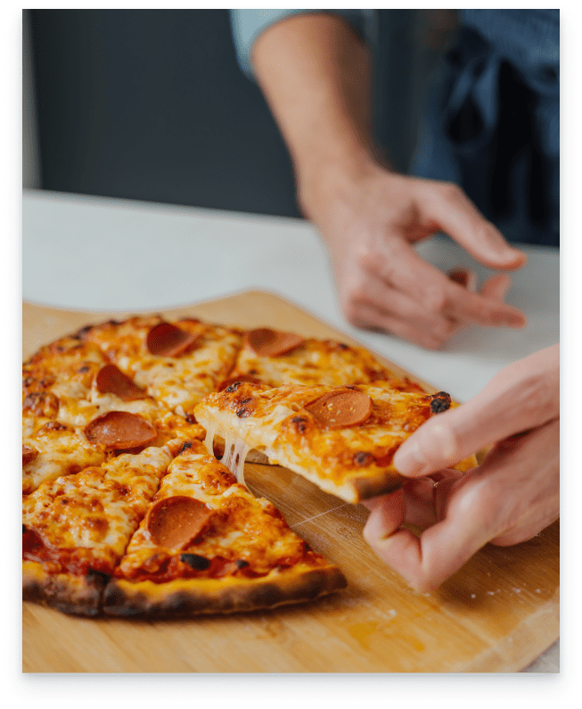 A fully cooked pizza has a slice being pulled away by Greg.